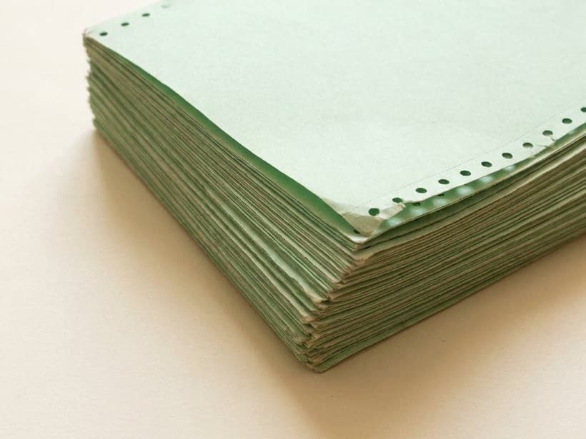 A thick stack of green computer printout paper with perforated feed-hole edges, on a pale ground.