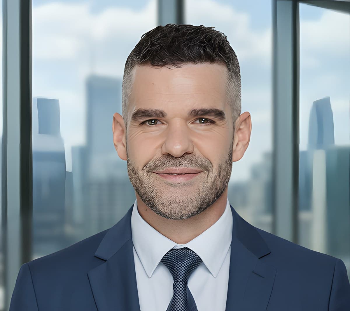 Head-and-shoulders portrait in a navy suit and tie, photographed against an office window with a city skyline behind.